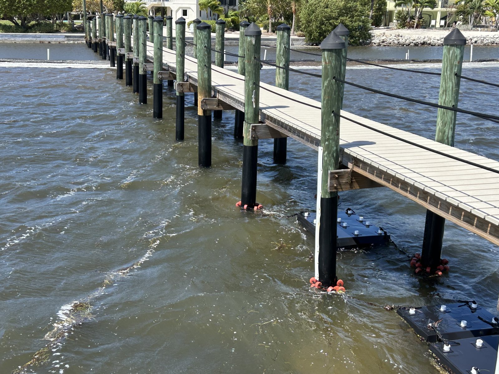 A long dock with its pilings wrapped in black protective barrier at the waterline, with Eco Habitats in the water beside it